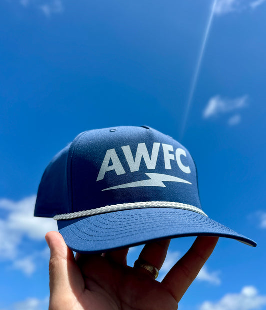 Blue cap with 'AWFC' logo held against a blue sky
